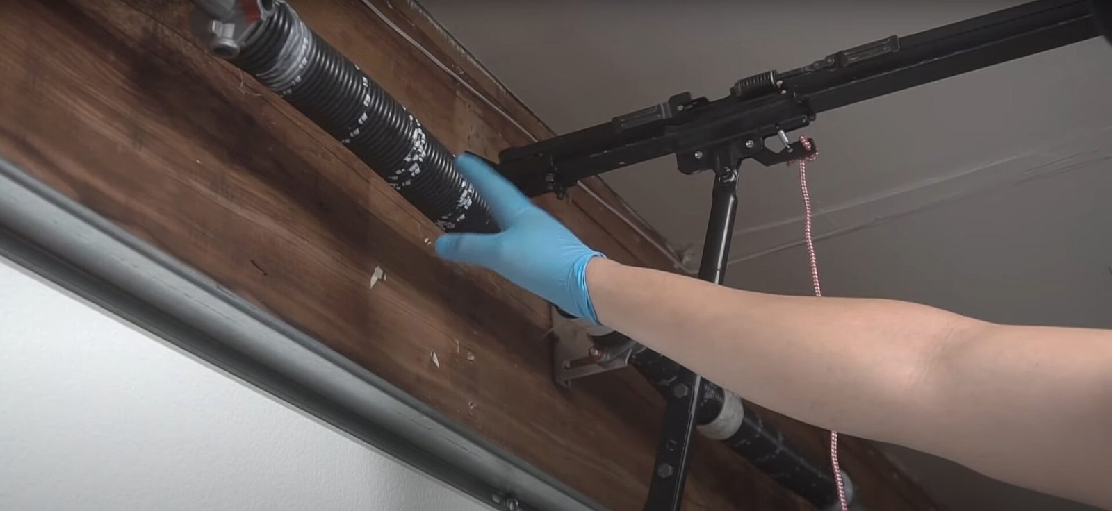 A professional technician repairing a garage door spring to improve energy efficiency in a residential home.